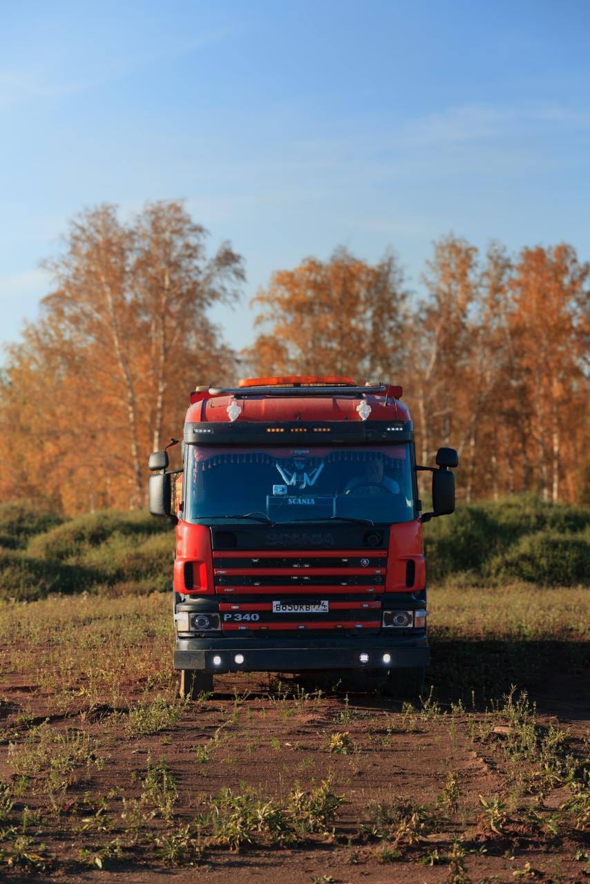 Эвакуатор Scania P340 спереди на грунтовой площадке, на фоне осенних берёз
