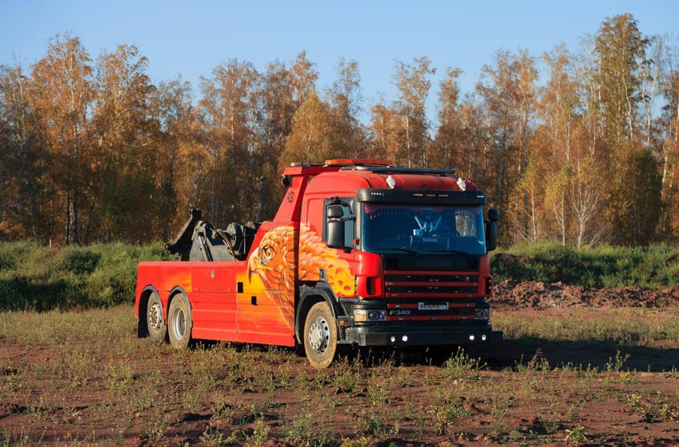 Красный эвакуатор Scania P340 с аэрографией орла, вид сбоку, на грунтовой площадке у осеннего леса
