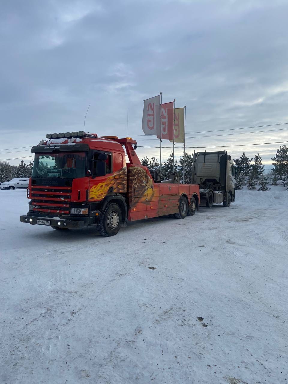 Эвакуатор Scania зимой буксирует седельный тягач на заснеженной площадке